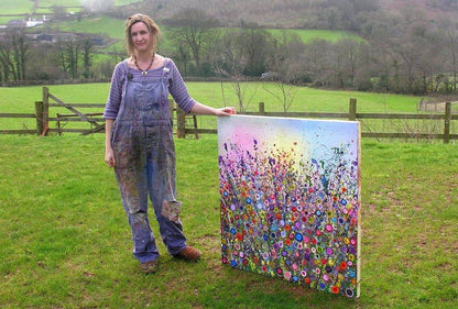 yvonne coomber stood in a field holding her artwork from the artists meadow seedballs available from beevive