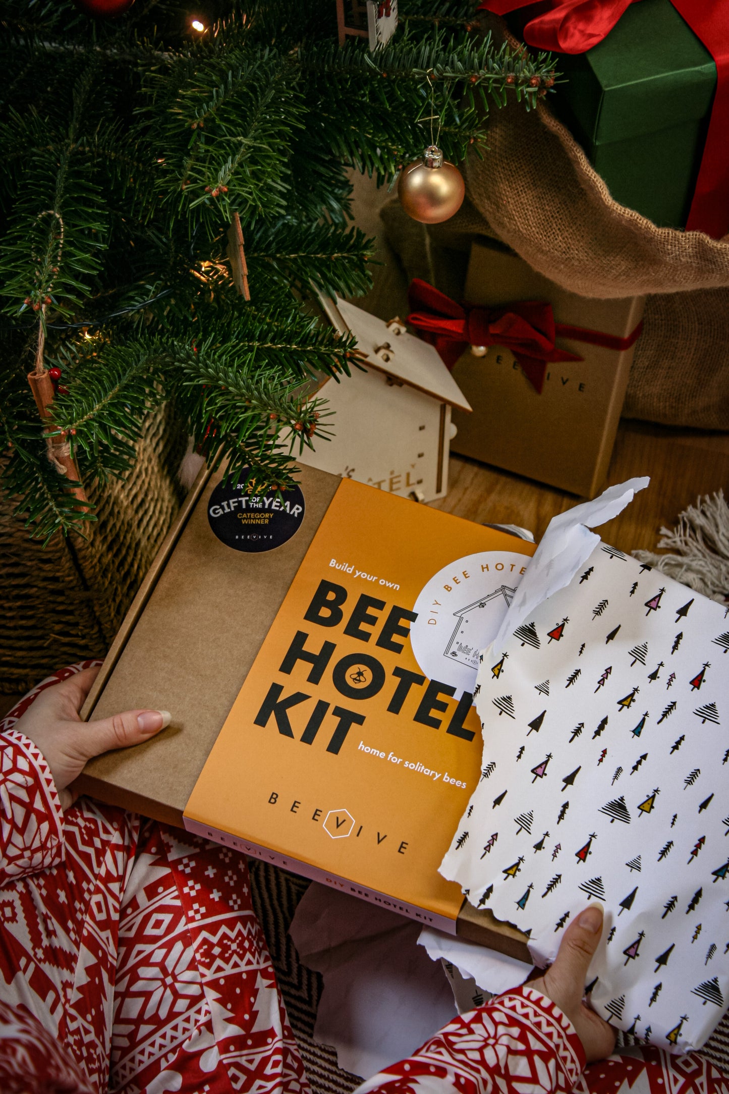 Bee Hotel Kit packaging with a person holding it near a Christmas tree and wrapped gifts.