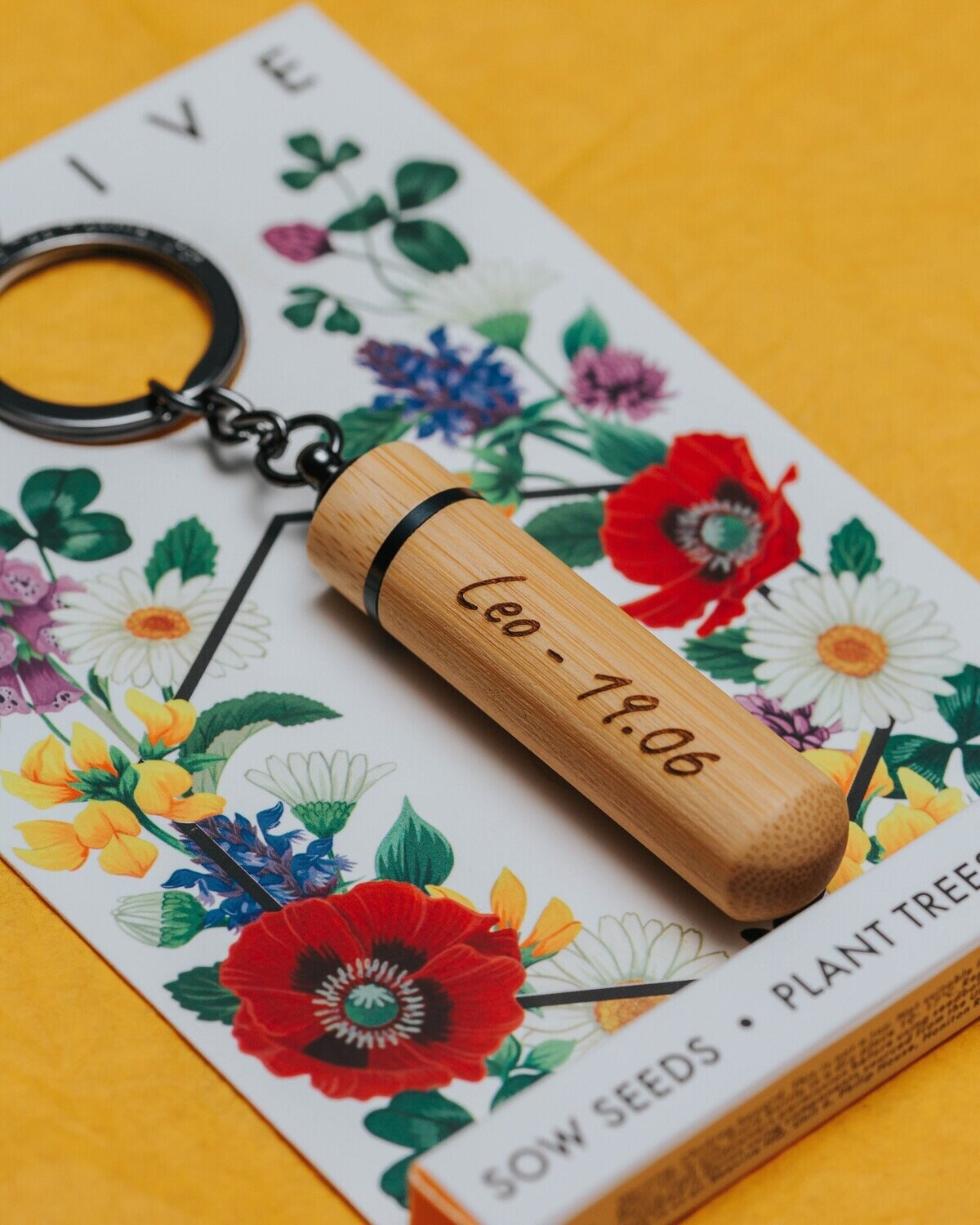 anthracite grey bamboo bee revival keyring in its packaging laying on an angled position on a yellow background