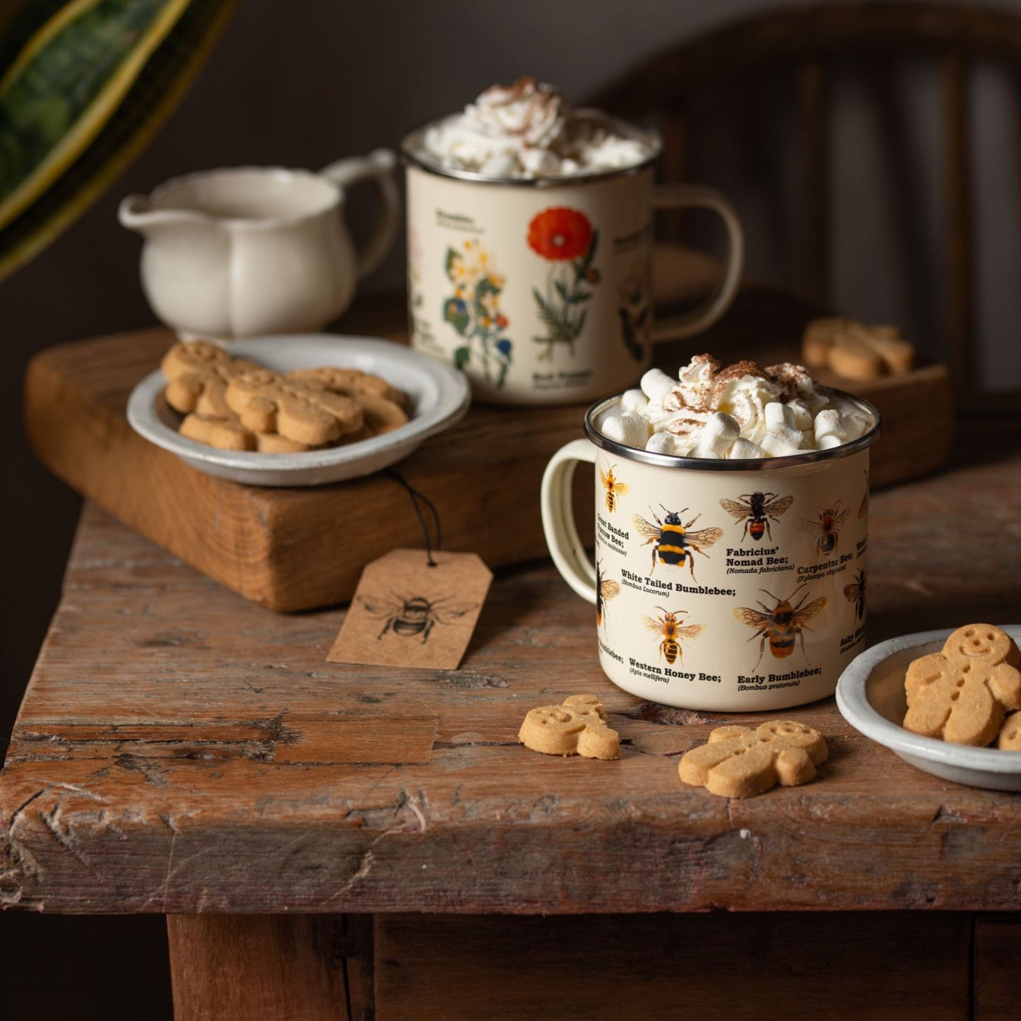 various bee species on enamel mug  on a wooden block with gingerbread men on a saucer alongside