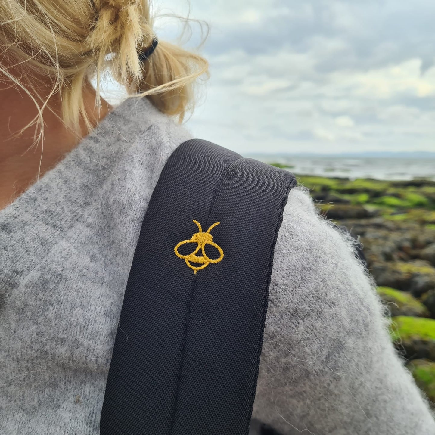 female with seaweed rocks in background - shot shows closeup of the yellow bee embroidered to the strap