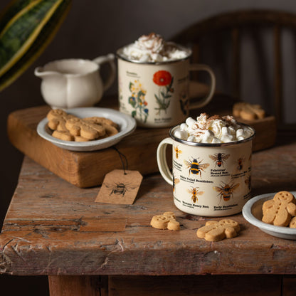 various bee species on enamel mug on a wooden block with gingerbread men on a saucer alongside